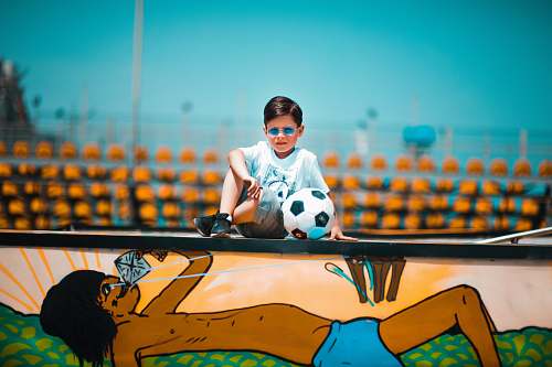 person boy sitting on graffiti wall beside soccer ball accessories