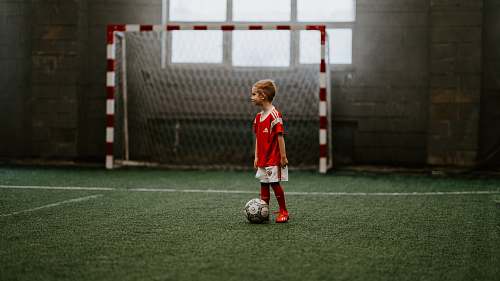 person boy standing beside soccer ball near soccer net football