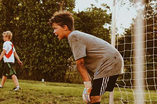 person boy wearing grey shirt standing near goalie net clothing