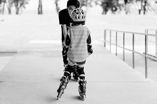 person grayscale photo of man and girl using inline skates near railings black-and-white