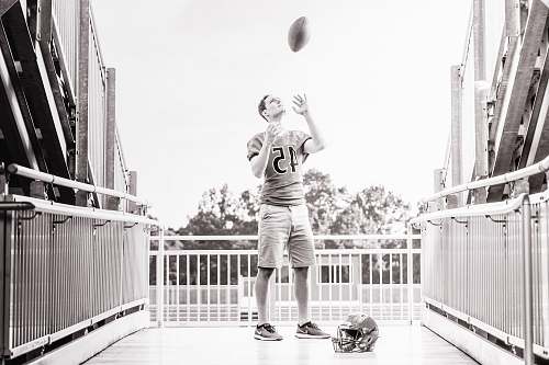 person grayscale photo of man standing while tossing football outdoors people