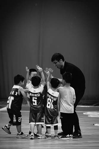 person grayscale photography of man standing beside kids wearing jersey shirts black-and-white