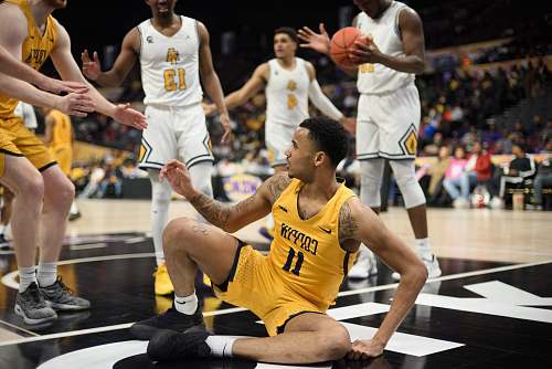 person man in yellow 11 basketball uniform sitting on middle of court surrounded by other players people
