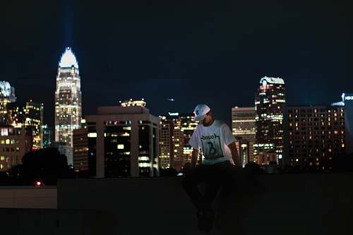 person man sitting on pavement with buildings during night time urban
