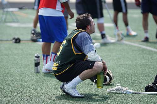 person man squat while holding water tumbler after playing lacrosse apparel