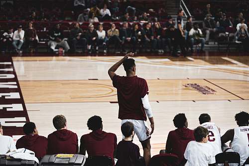 person man standing while other players sitting near basketball court people
