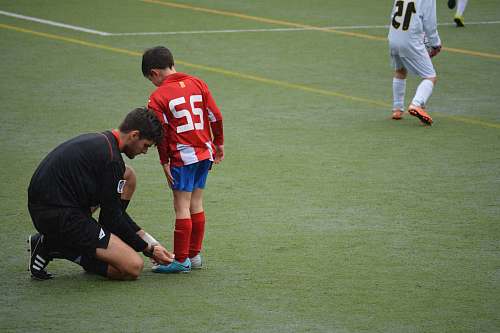 people man tying boy's shoes on field football