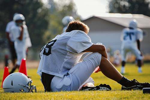 person selective focus photography of man sitting on field wearing football gear people