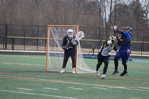 person three people playing lacrosse on green field near goal net people