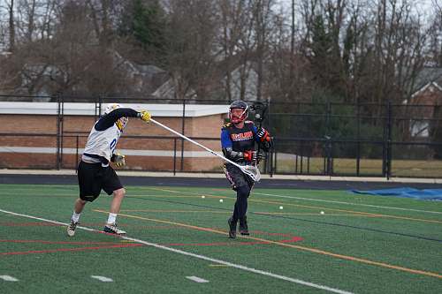 person two men playing lacrosse on green field field