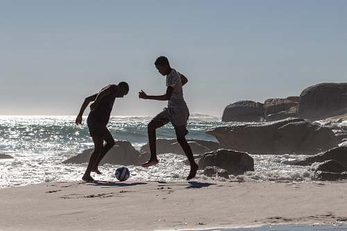 person two men playing with soccer ball near seashore soccer