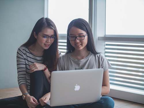 laptop two smiling women starring on silver MacBook inside well-lit room computer