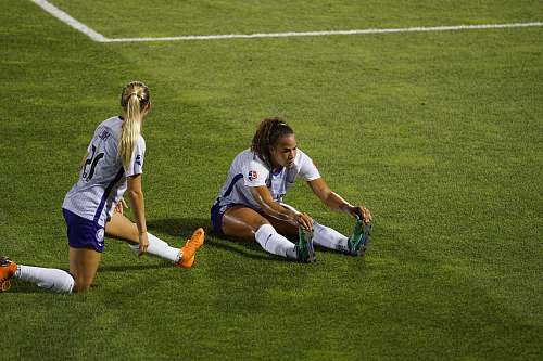 person two women soccer players stretching legs on lawn people