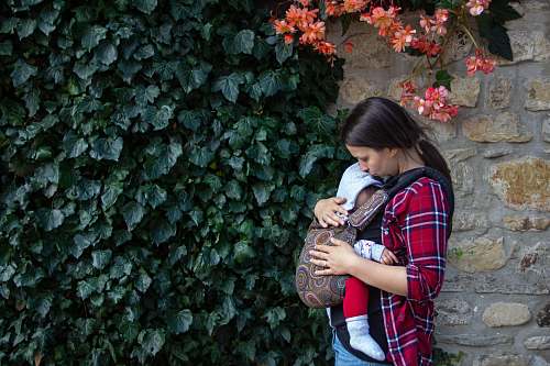 apparel woman carrying baby near hedge clothing