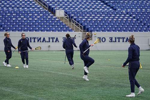 person women playing lacrosse on green field during daytime field