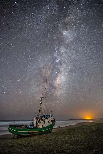astronomy green and white fishing boat on gray sand under white and gray sky milky way
