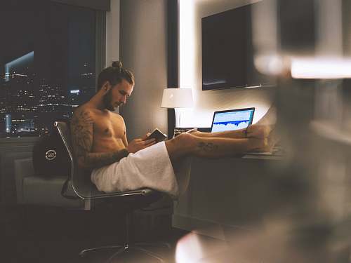 human man sitting on rolling chair while using smartphone laptop