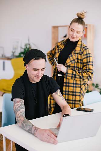 human man using laptop beside woman holding pen skin