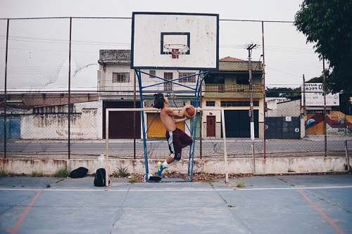 human man wearing brown shorts doing lay-up near basketball ring during daytime people