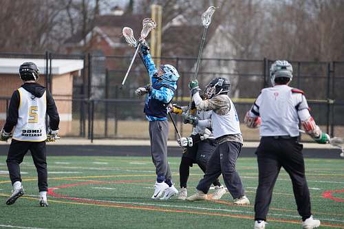 human people playing lacrosse on green field during daytime apparel