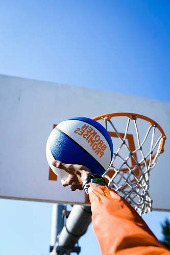 human person holding basketball facing towards basketball hoop people