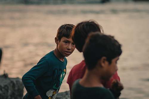 human three boys standing near body of water during daytime clothing