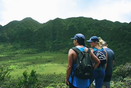 human three women standing with a view of green mountain under gray sky people