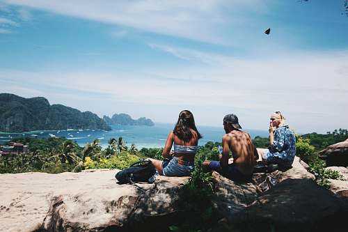 human topless man sitting between two persons near body of water back
