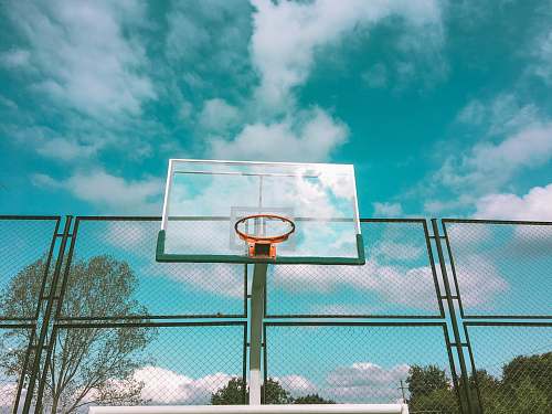 sports green and orange basketball hoop near green chain link fence under white and blue skies during daytime team