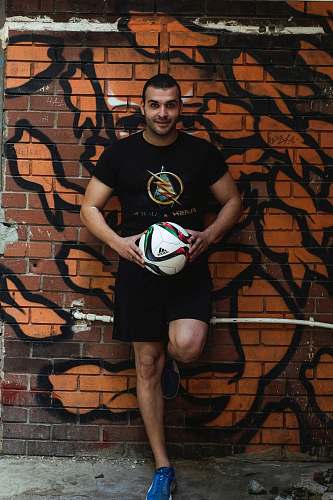 football man leaning on wall holding velleyball ball