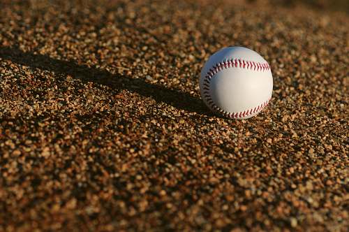 sports white and red baseball on brown soil at daytime baseball