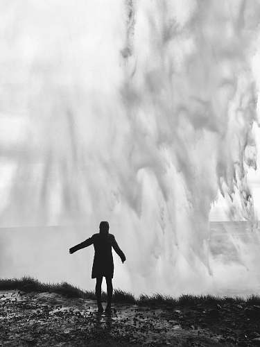 person grayscale photography of person standing in front of splashing water waves grey