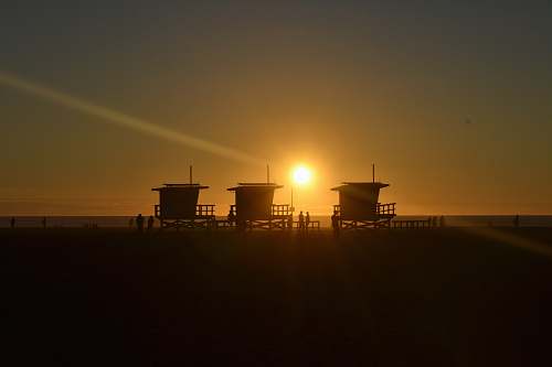 dawn silhouette of three cottages on the beach sunrise