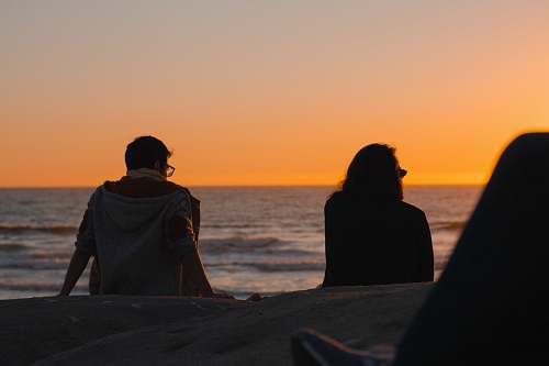 person man and woman sitting near ocean silhouette