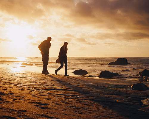 person man and woman walking on seashore during sunset standing