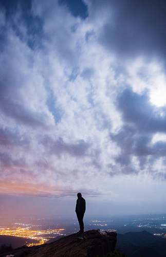 person man standing on cliff with cityscape view under cloudy sky nature