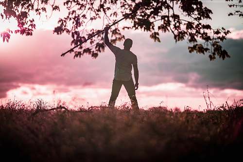 person man standing wearing white t-shirt and black pants raising right hand during daytime standing