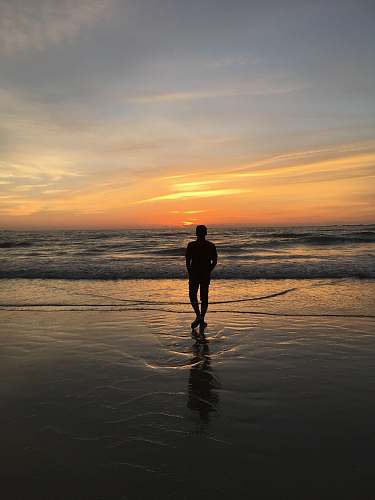 person silhouette of man standing on seashore standing