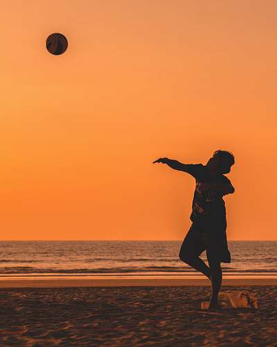 people silhouette of man throwing ball near ocean at golden hour person