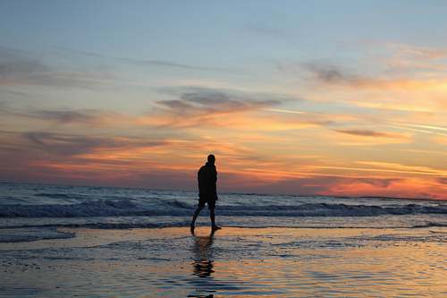 person silhouette of man walking on seashore standing