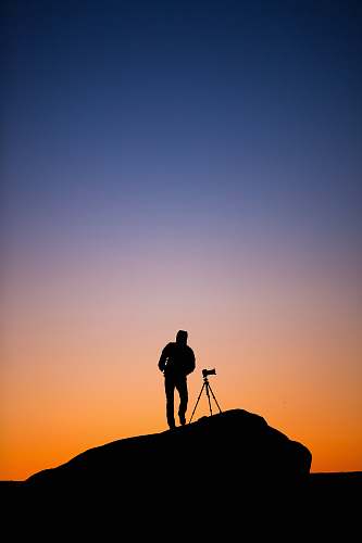 person silhouette of person standing beside DSLR camera with stand at sunset tripod