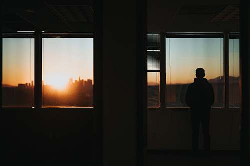 person silhouette of person standing in front of window during golden hour people