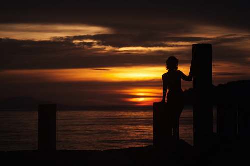 person silhouette of woman on dock during orange sunset people