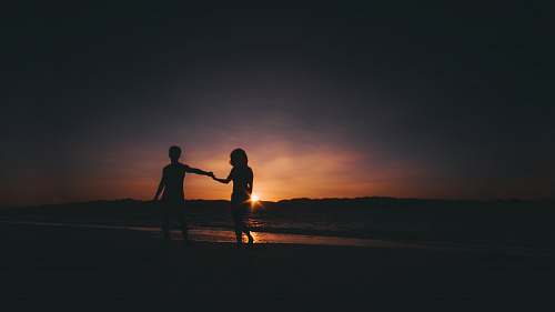 person silhouette photo of couple beside sea holding hands