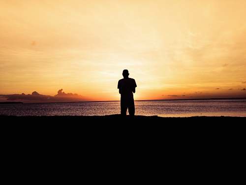 person silhouette photo of person standing in front of body of water during sunset standing