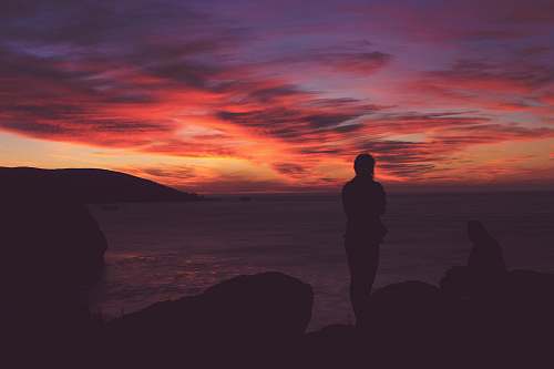 person silhouette photo of person standing near sea during golden hour people