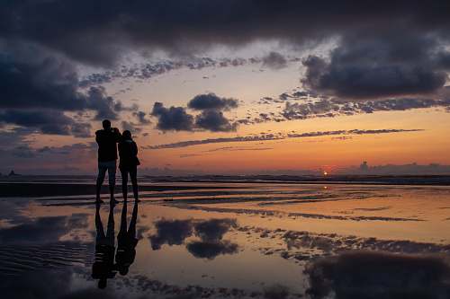 person silhouette photography of man and woman standing on seashore during golden hour nature