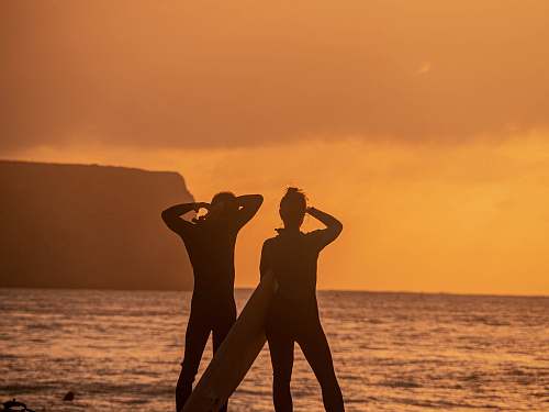 person silhoutte of person wearing wetsuit holding white surfboard standing on seashore during sunset sneery standing