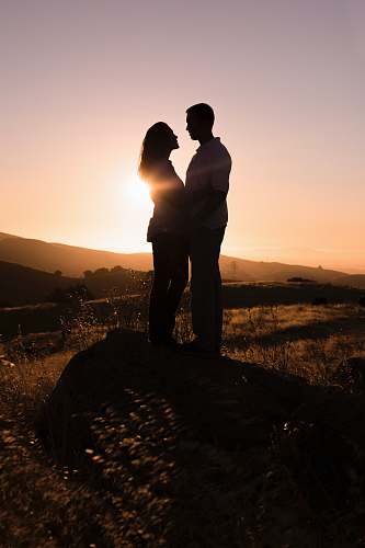 human man and woman standing on rock facing each other during day person