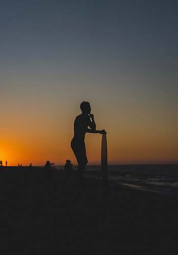 outdoors person standing and holding surfboard on shore during golden hour human